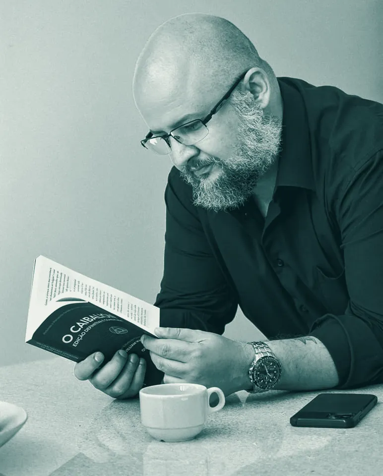 Gogo Cristo Neto lendo um livro, concentrado, com uma xícara de café à frente